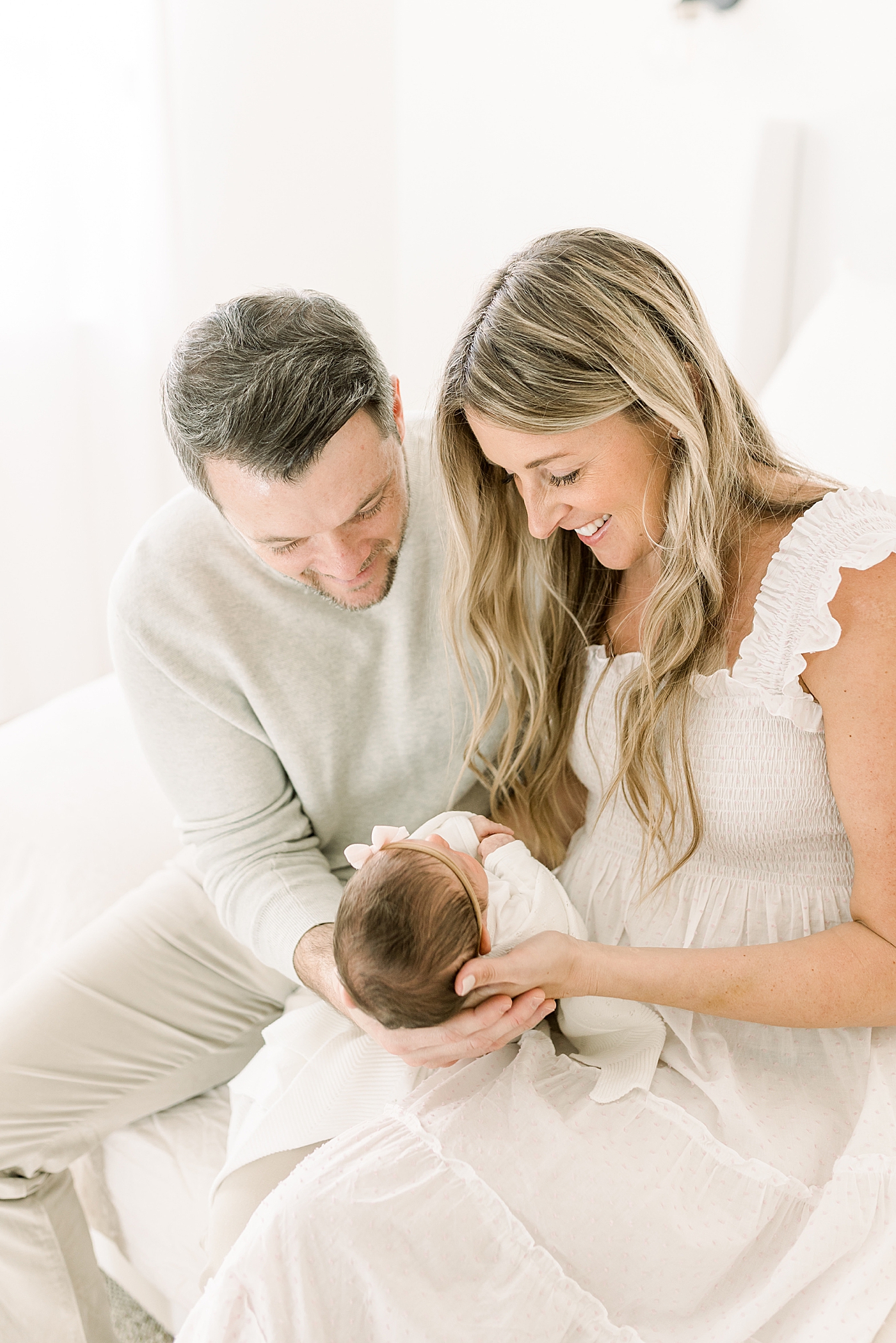 Mom and dad sitting in a white chair holding their newborn | Newborn Photos with Toddler with Caitlyn Motycka Photography