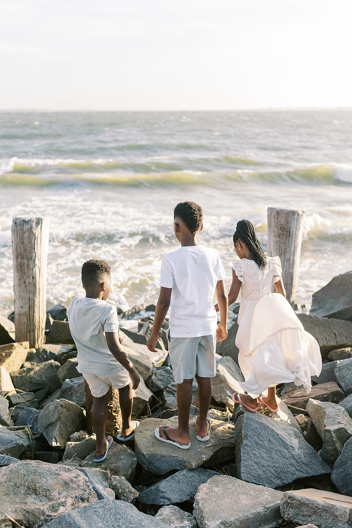 Three siblings walking on rocks during beach family photos in Charleston | Image by Caitlyn Motycka