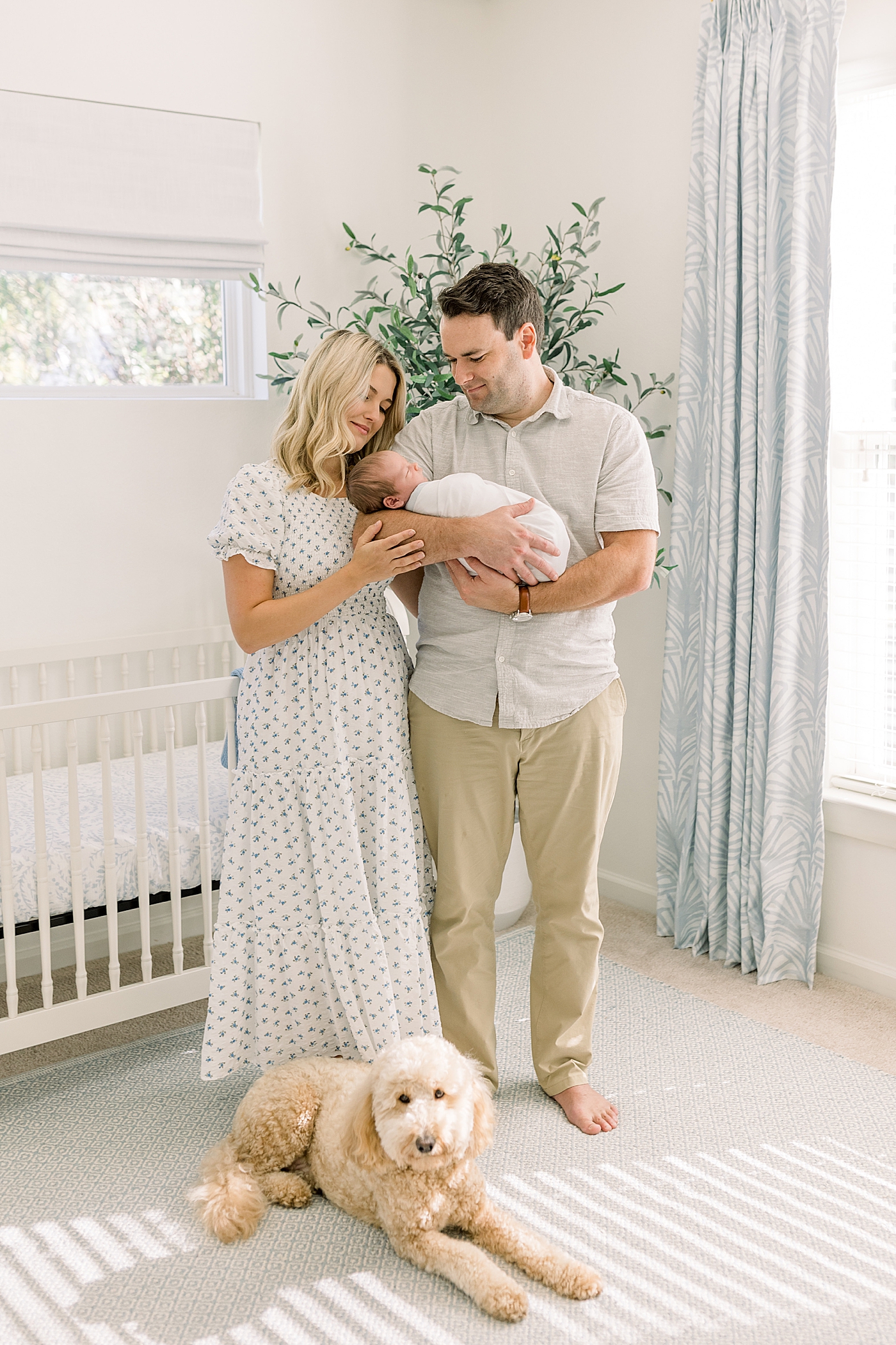 Parents holding a newborn swaddled in their arms while dog lays at their feet during baby boy newborn session | Image by Caitlyn Motycka Photography