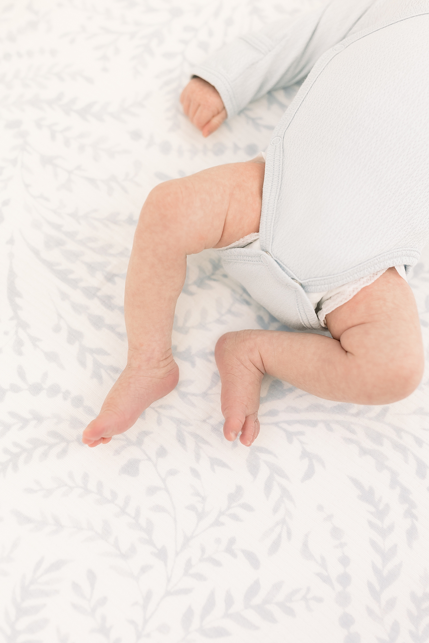 Overhead vignette of baby feet in a light blue onesie and soft light during baby boy newborn session | Image by Caitlyn Motycka Photography