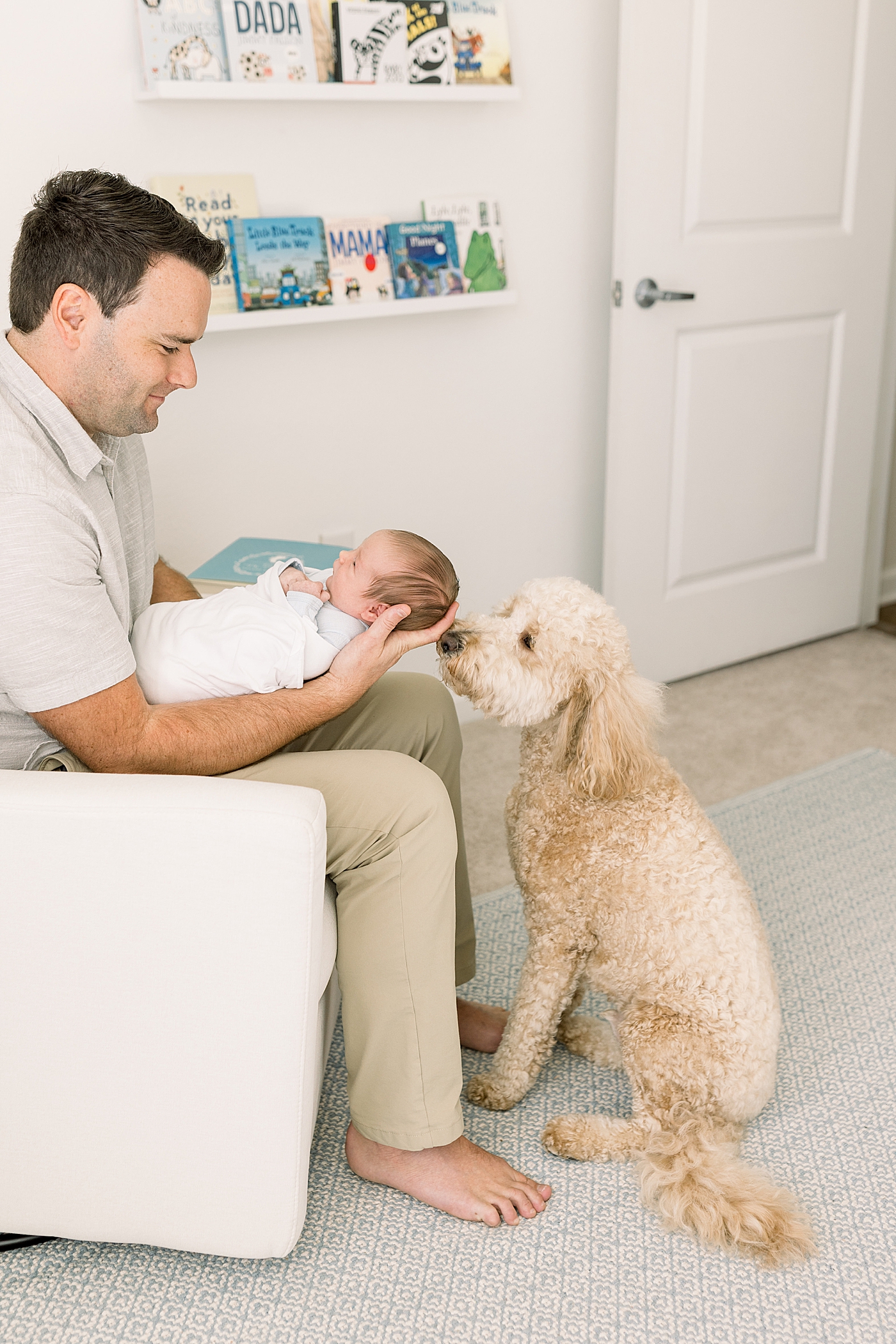 Dad holding his newborn while sitting in a corner rocking chair with the family dog at his feet | Image by Caitlyn Motycka Photography