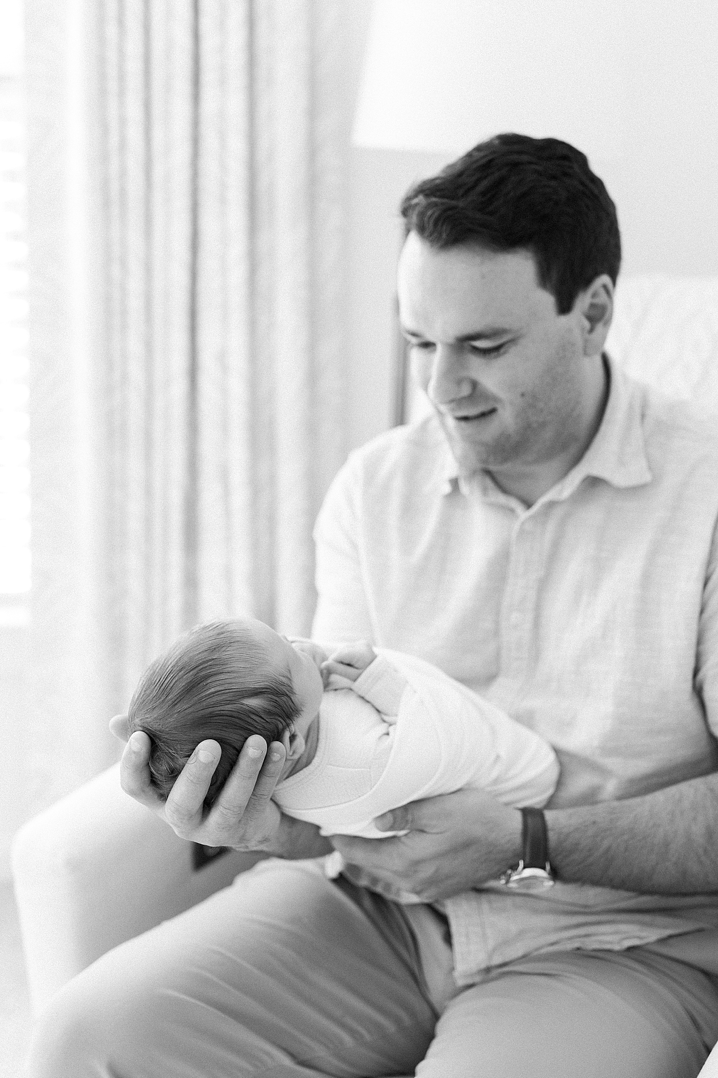 Black and white image of dad holding newborn while sitting in a corner rocking chair | Image by Caitlyn Motycka Photography