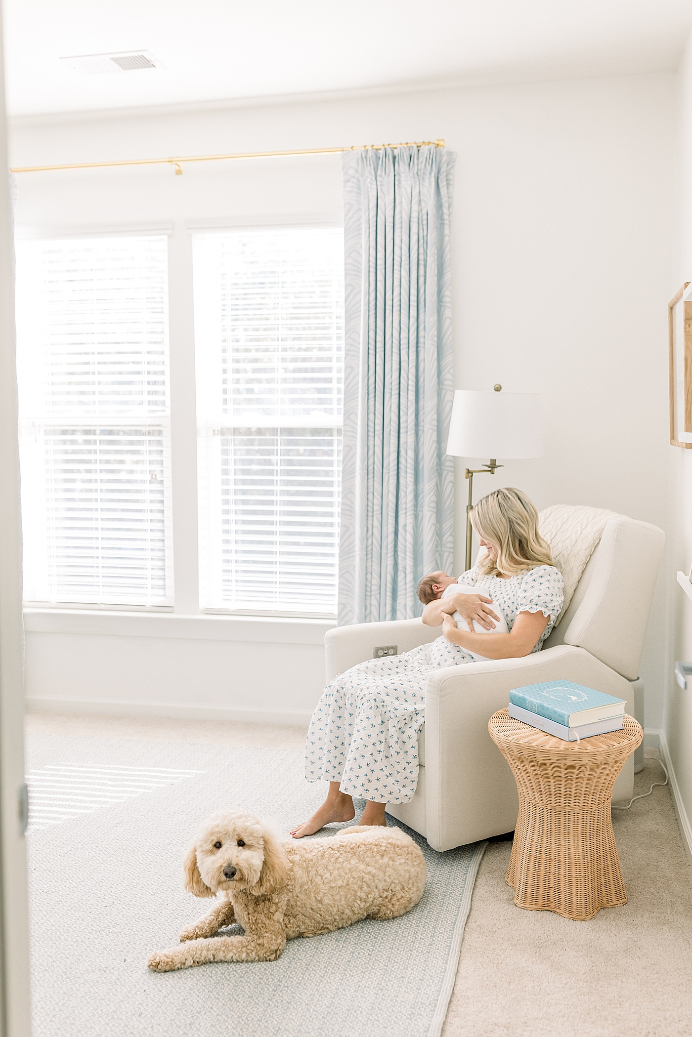 Mother holding her baby while sitting in a corner rocking chair with the family dog at her feet | Image by Caitlyn Motycka Photography