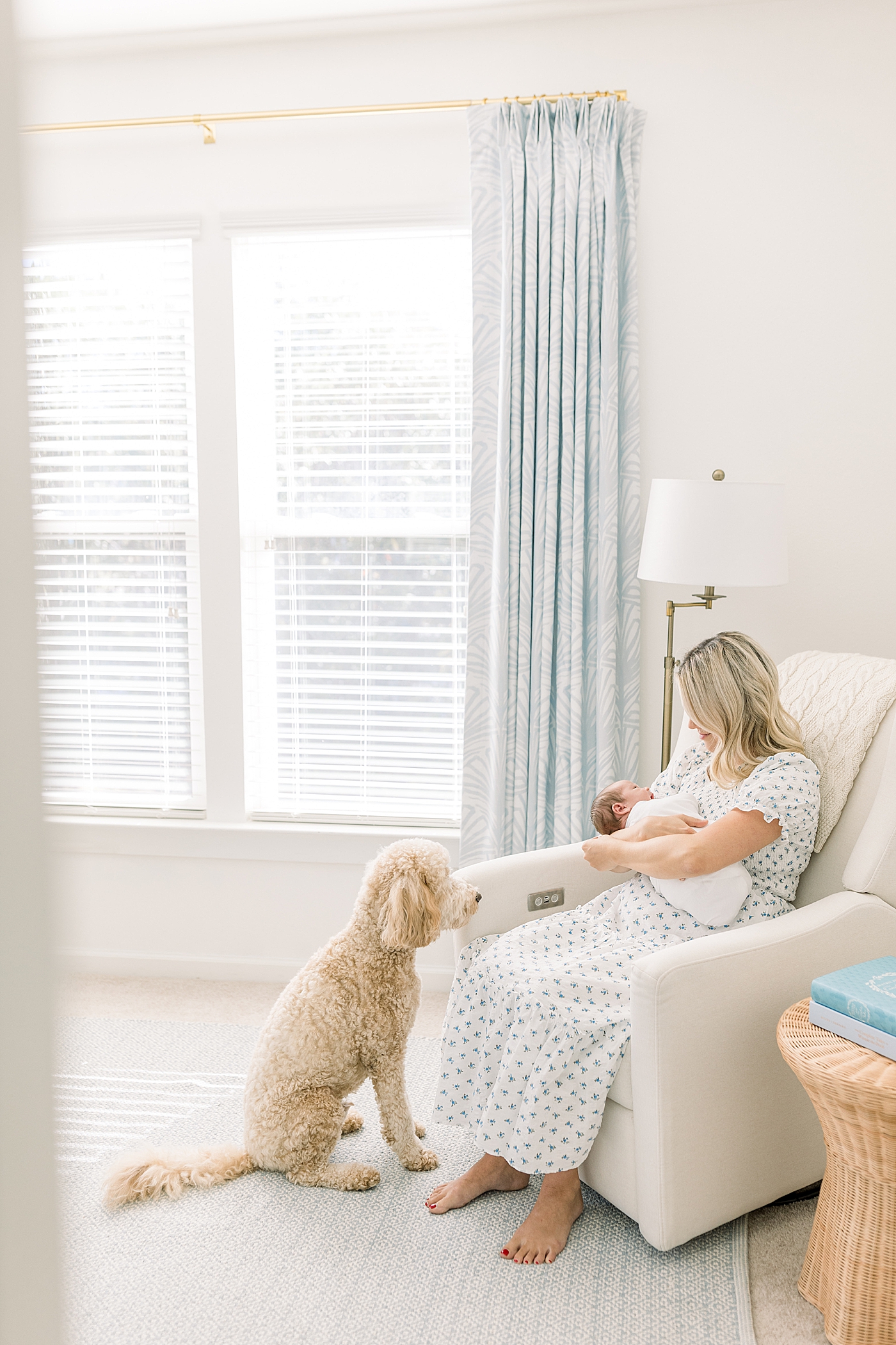 Mother holding her baby while sitting in a corner rocking chair with the family dog at her feet during baby boy newborn session | Image by Caitlyn Motycka Photography