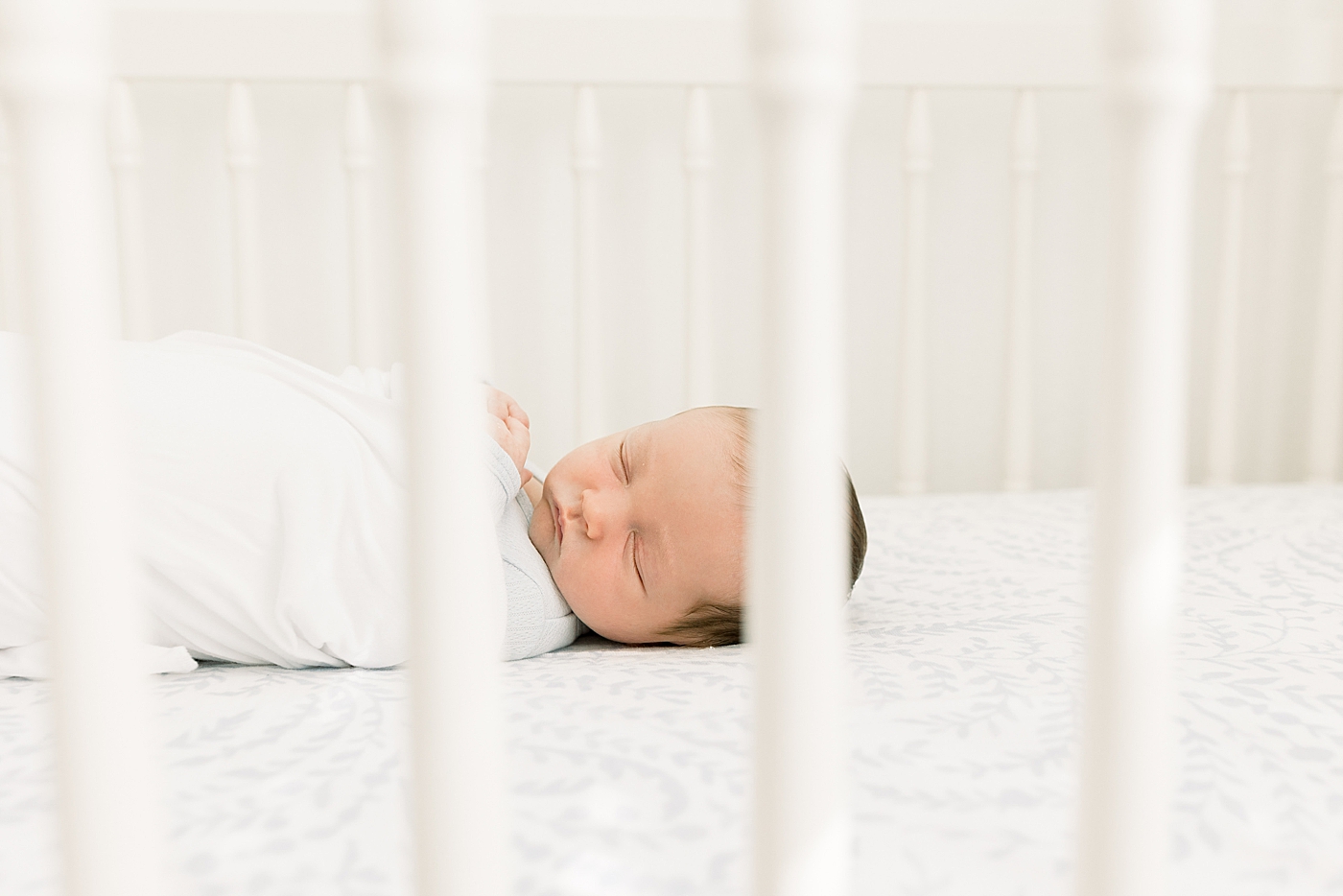 Close up of a newborn swaddled in a white crib during baby boy newborn session | Image by Caitlyn Motycka Photography