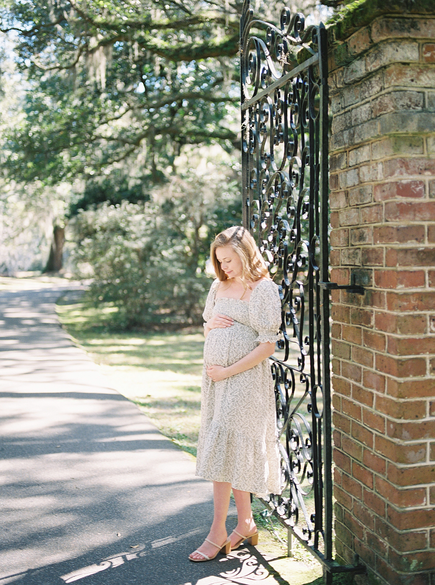 Woman in a spring dress holding her pregnant belly next to an iron gate | Image by Caitlyn Motycka Photography