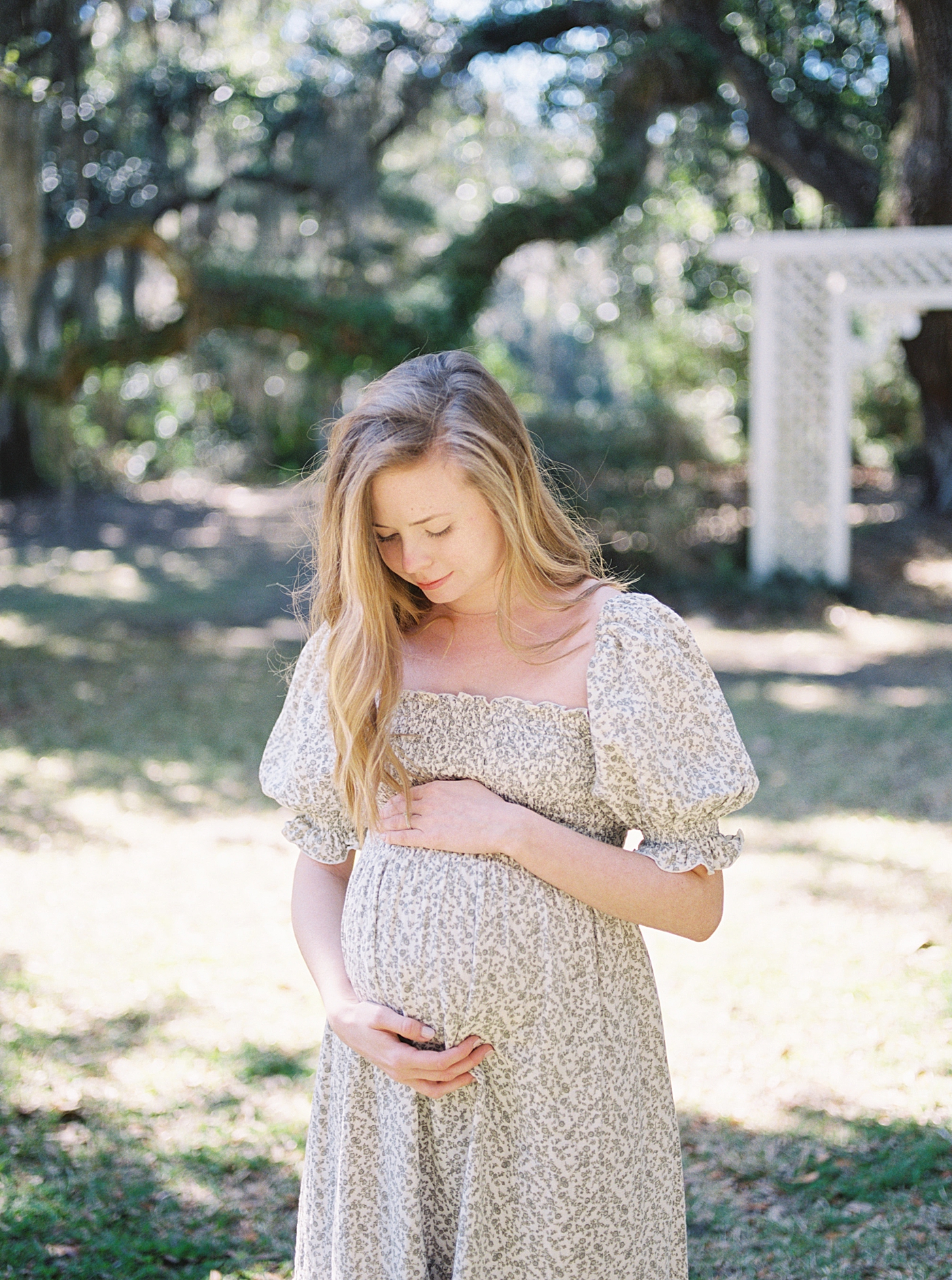 Woman in a spring dress holding her pregnant belly during their Maternity Session at Charlestowne Landing| Image by Caitlyn Motycka Photography