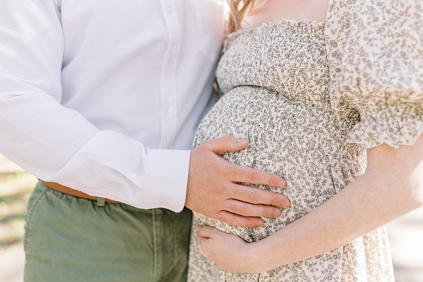Close up image of husband and expecting wife in a spring dress holding her pregnant belly | Image by Caitlyn Motycka Photography