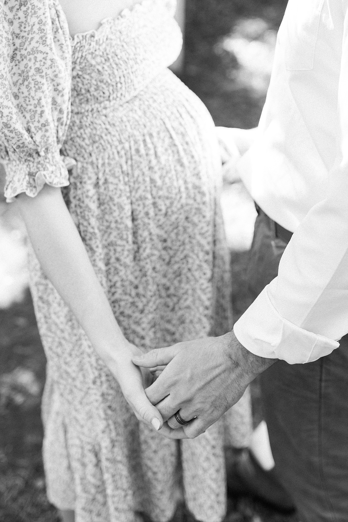 Black and white image of expecting wife in a spring dress holding hands with her husband | Image by Caitlyn Motycka Photography