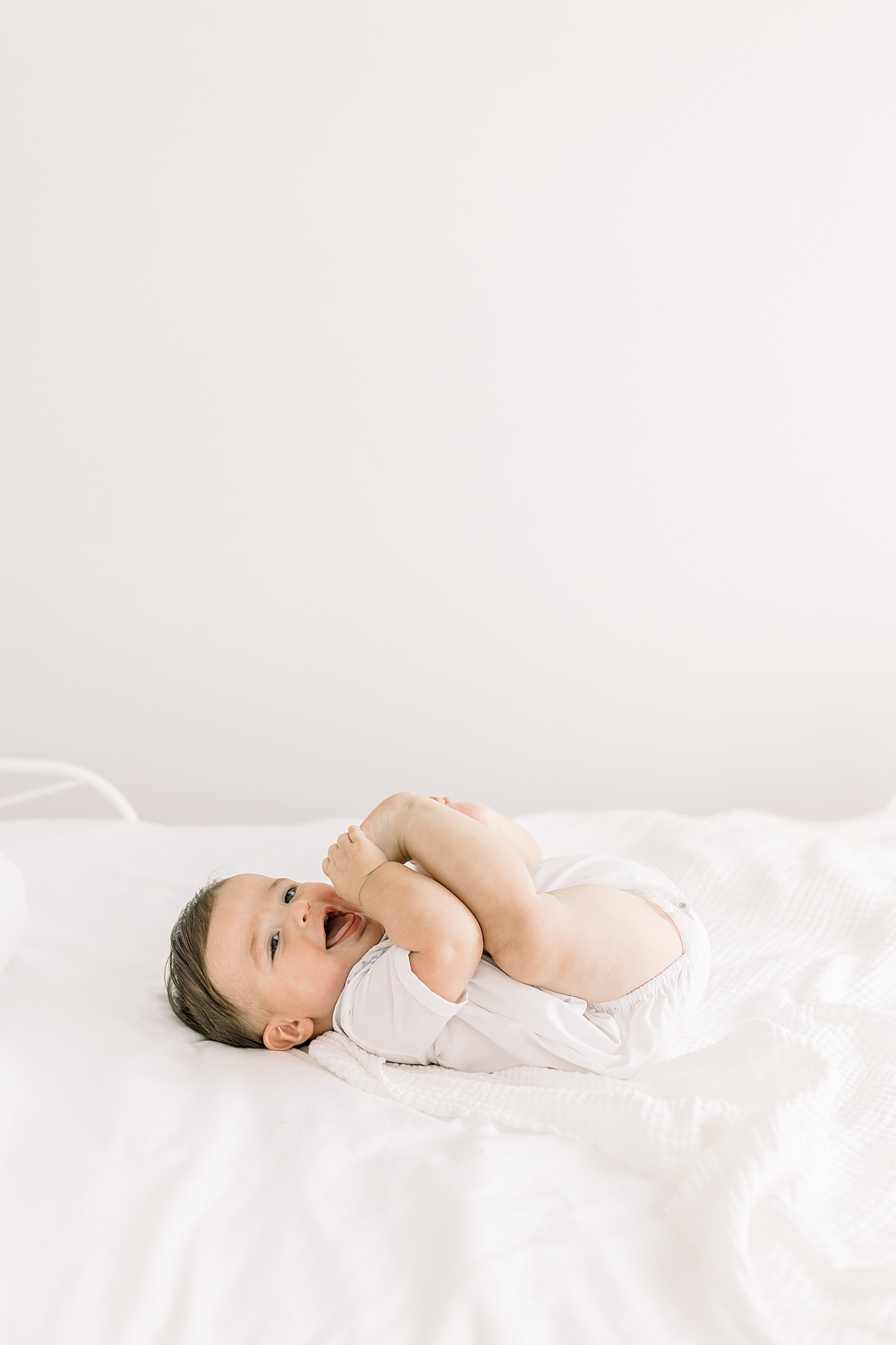 Baby smiling and laying on back, chewing on feet in a softly lit room | Images by Caitlyn Motycka