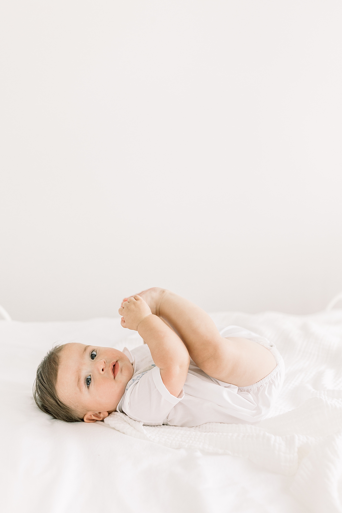 Baby smiling and laying on back, looking at camera in a softly lit room | Images by Caitlyn Motycka