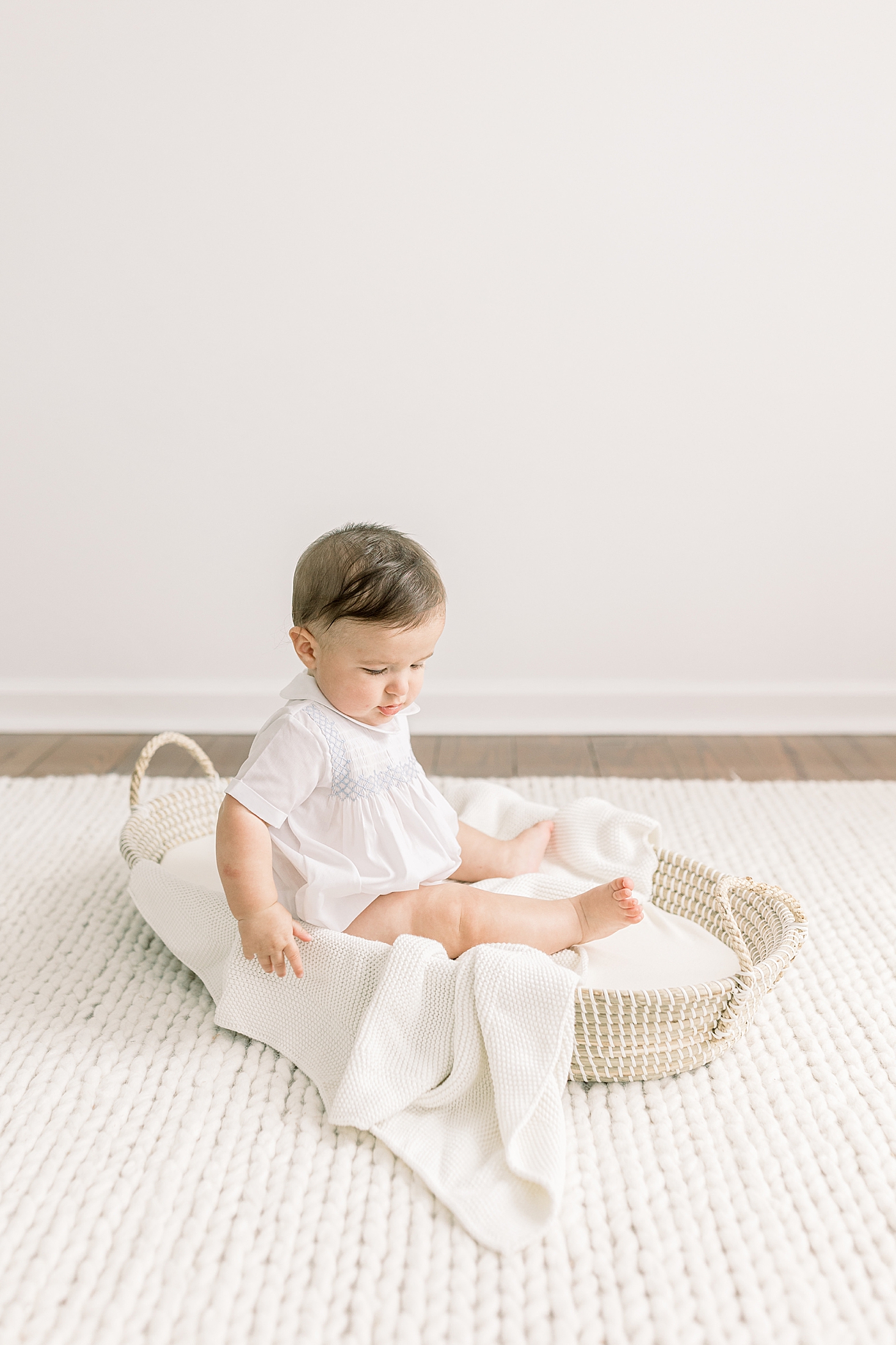 Baby sitting up in a shallow basket on a white rug in a white room during Studio Milestone Session | Images by Caitlyn Motycka