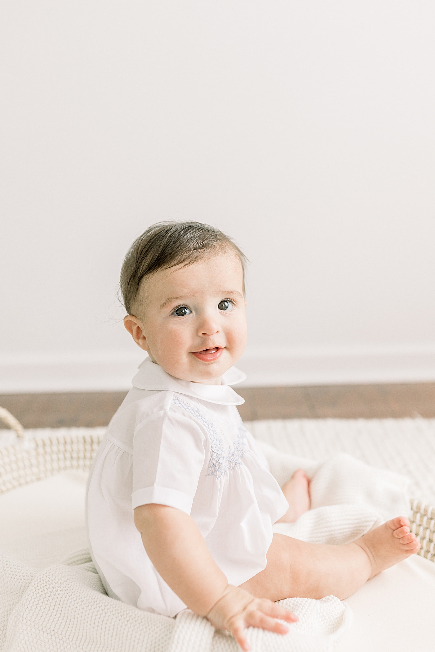 Baby sitting up in a shallow basket on a white rug in a white room | Images by Caitlyn Motycka