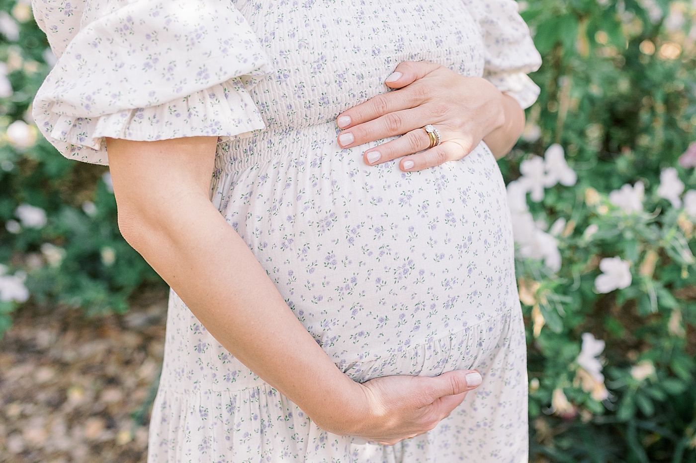Close up of an expecting mother standing beside a home with flowers holding her stomach during Spring Motherhood Minis in Charleston | Image by Caitlyn Motycka