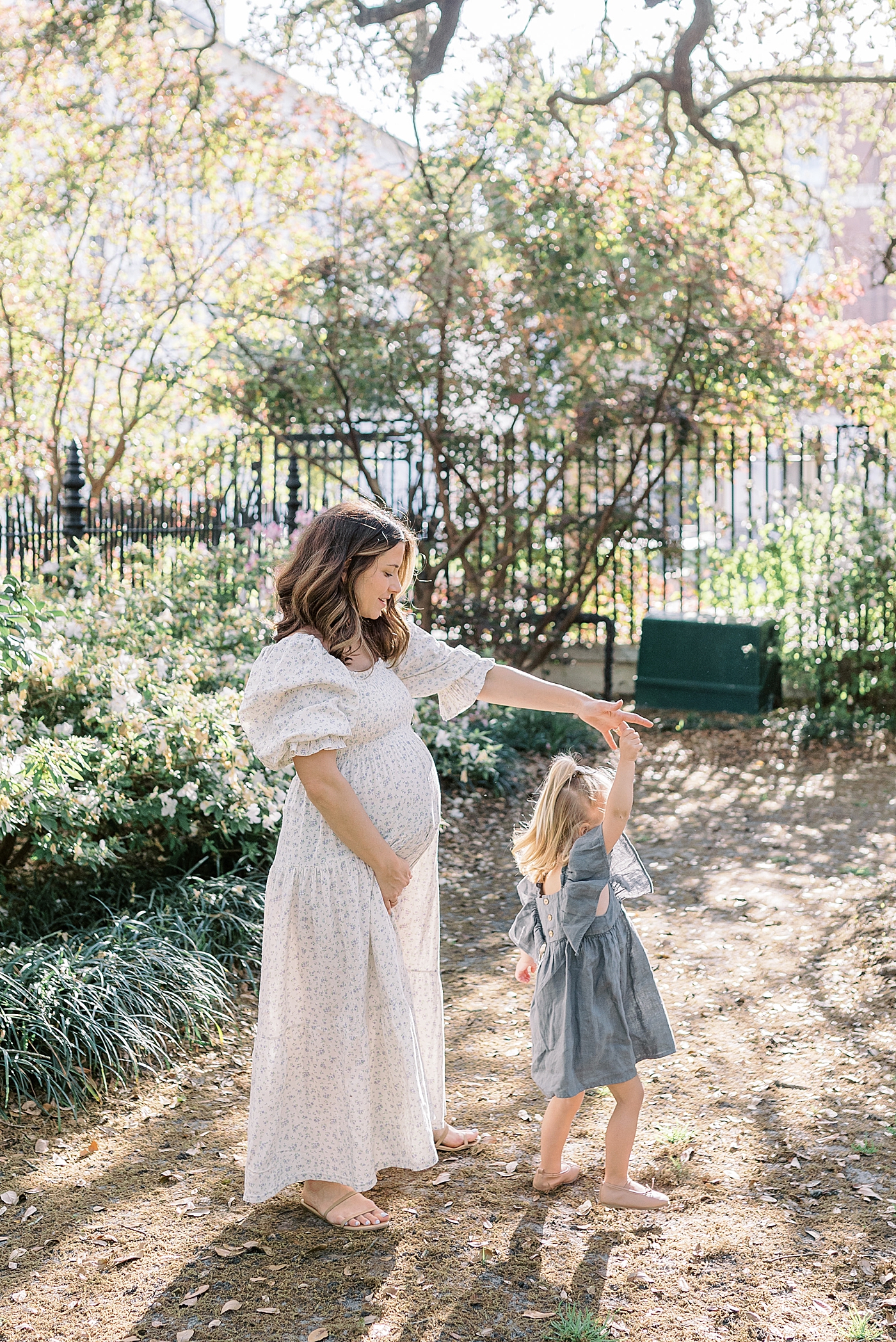 Expecting mother spinning her daughter in a garden with an iron gate | Image by Caitlyn Motycka