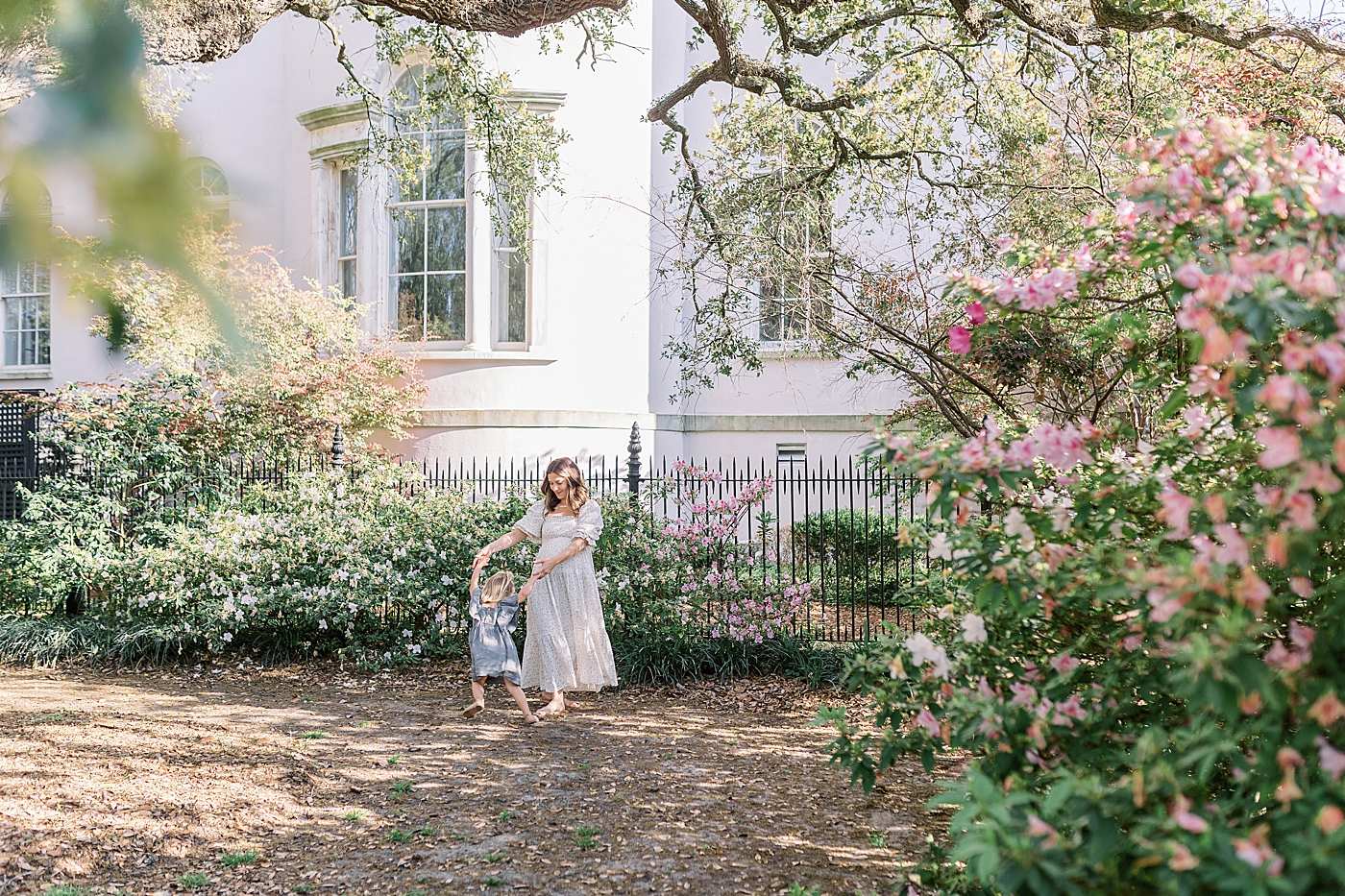 Expecting mother dancing with her daughter in a Charleston garden with an iron gate | Image by Caitlyn Motycka