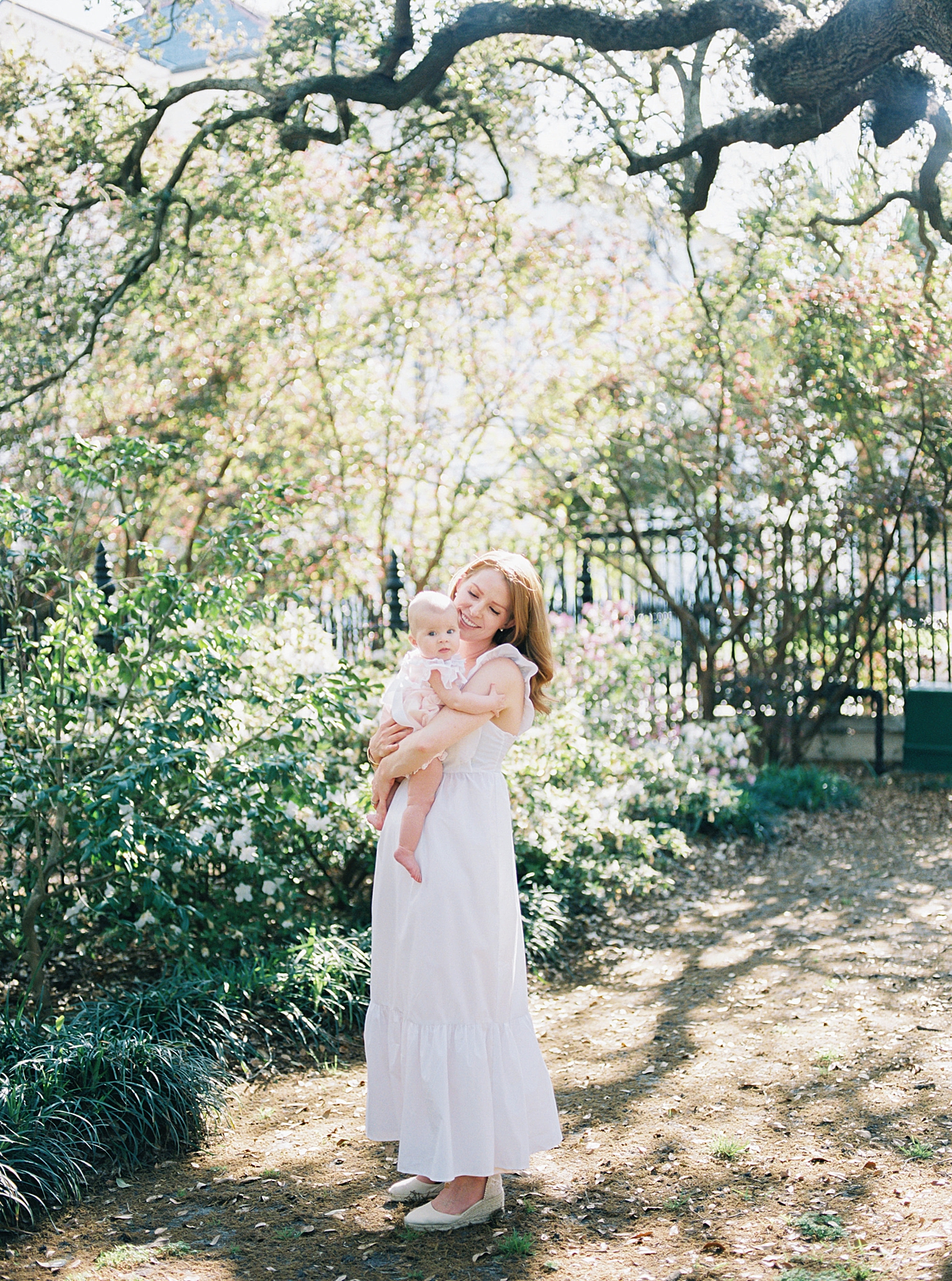 Mother in a spring dress holding her baby in a garden during Spring Motherhood Minis in Charleston | Image by Caitlyn Motycka