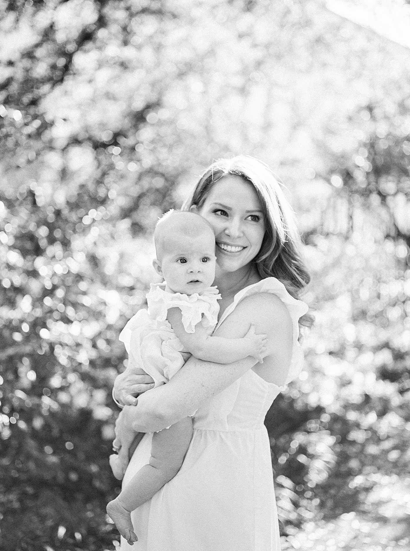 Black and white image of a mother in a spring dress holding her baby in a garden during Spring Motherhood Minis in Charleston | Image by Caitlyn Motycka