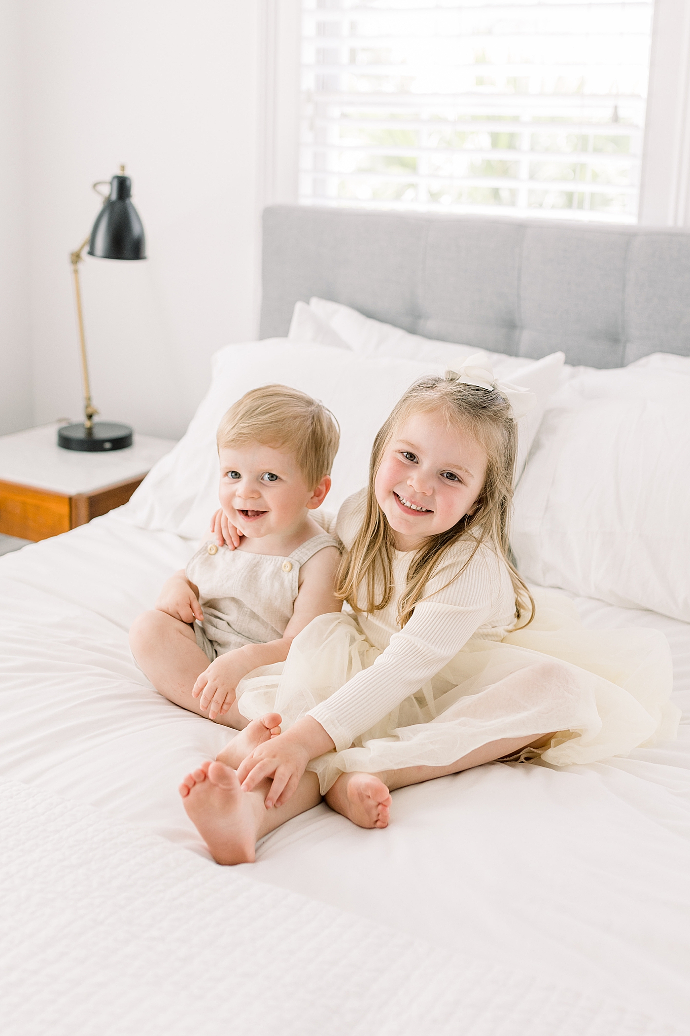 Young girl with her arm around her little brother sitting bed, smiling and looking at the camera | Image by Caitlyn Motycka 