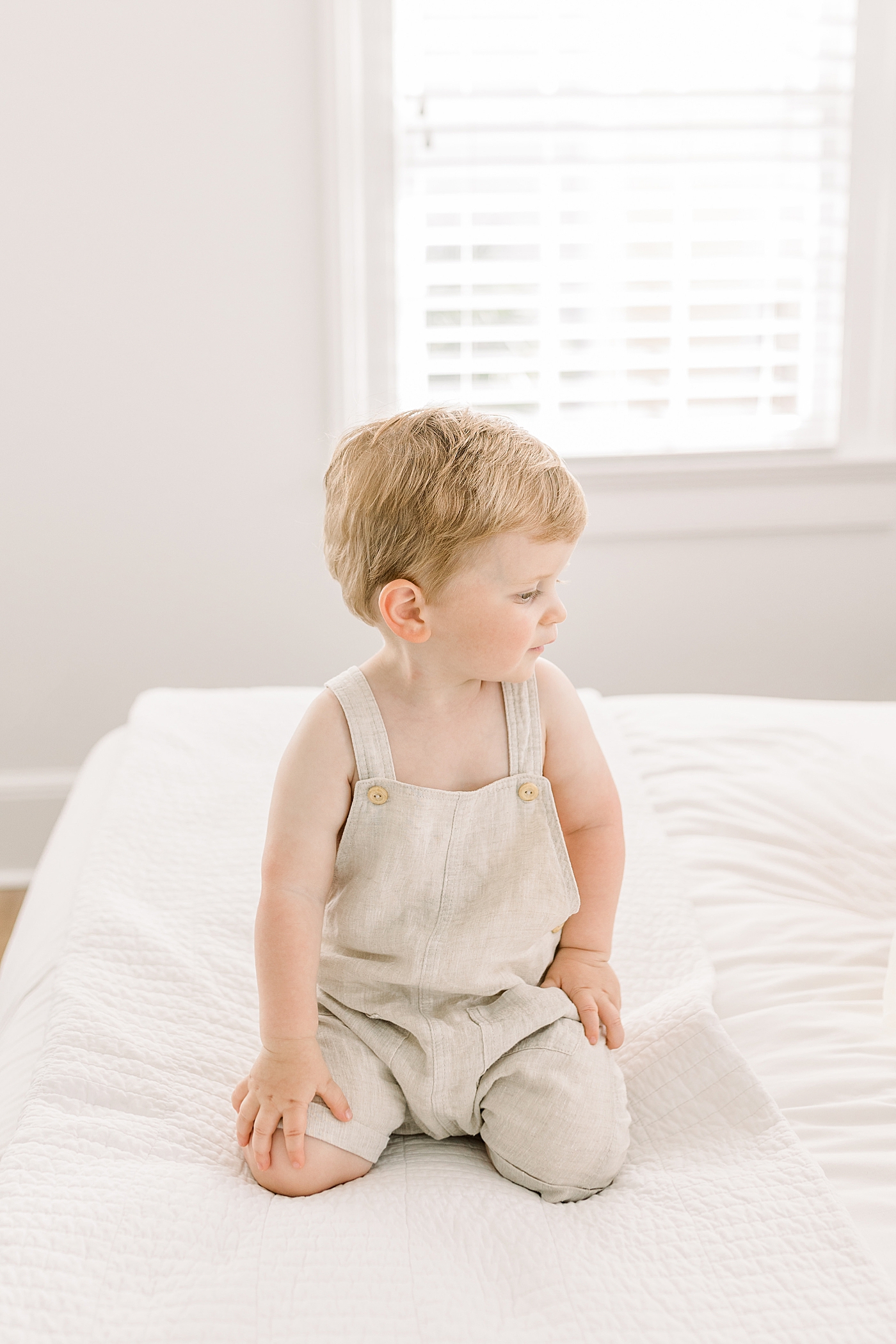 Little boy kneeling and looking sideways in a softly lit, white room | Image by Caitlyn Motycka 