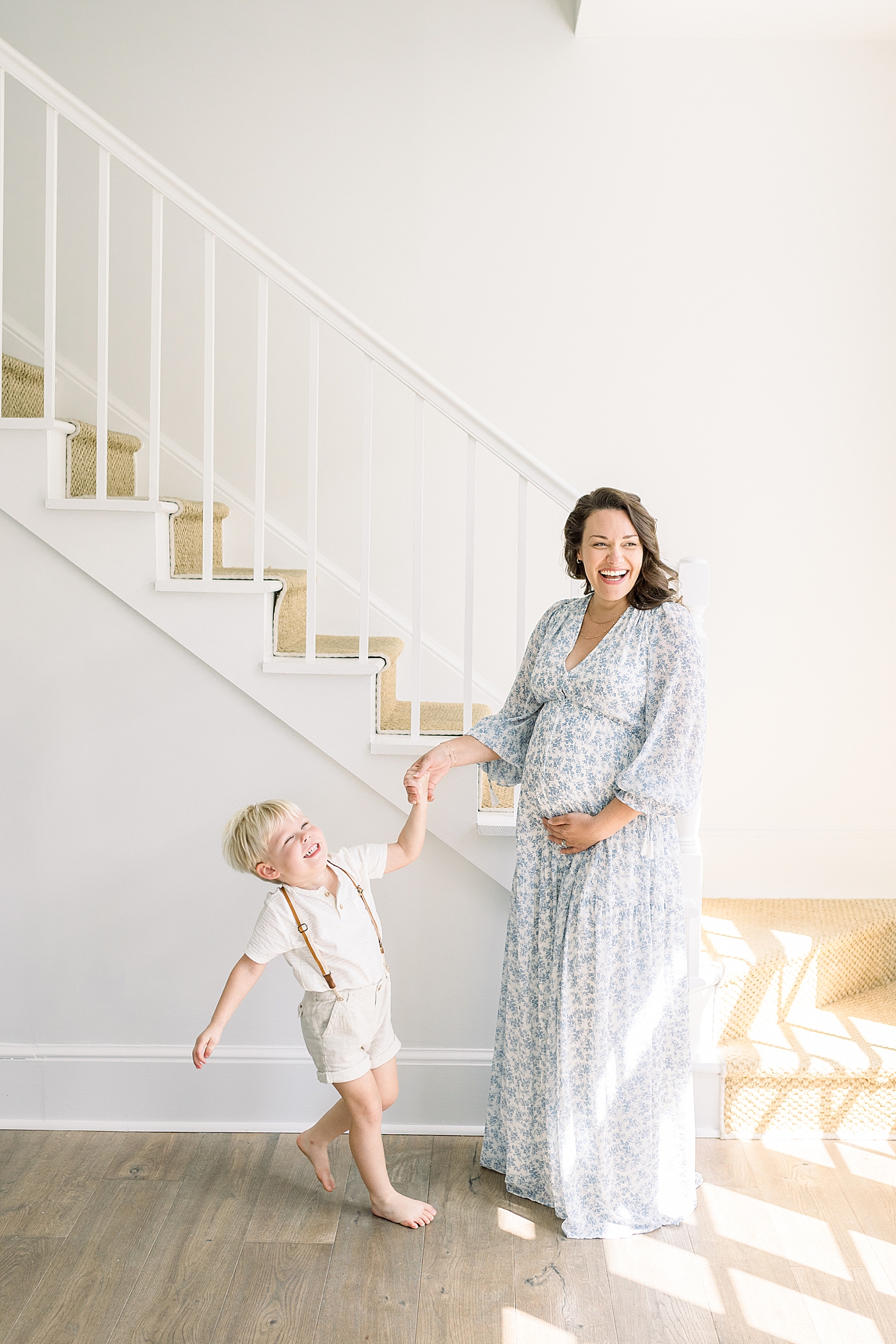 Mother and son smiling, laughing, dancing in an all white entry way next to a staircase | Image by Caitlyn Motycka 