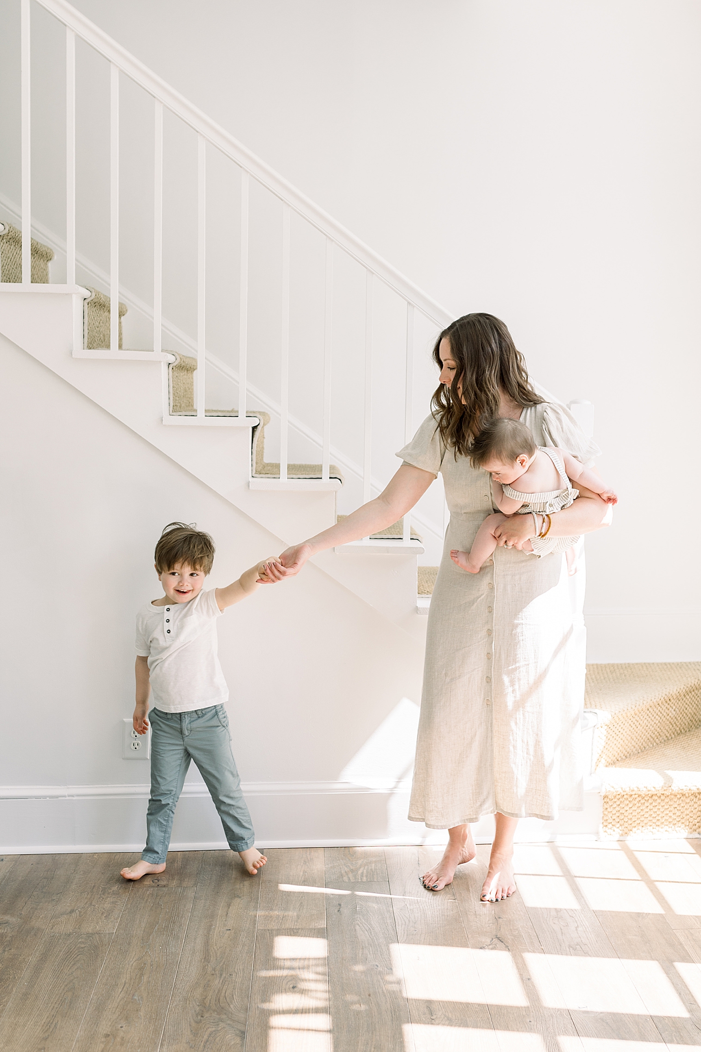Mother holding her baby and the hand of her young son in a white, simple entry way | Image by Caitlyn Motycka 