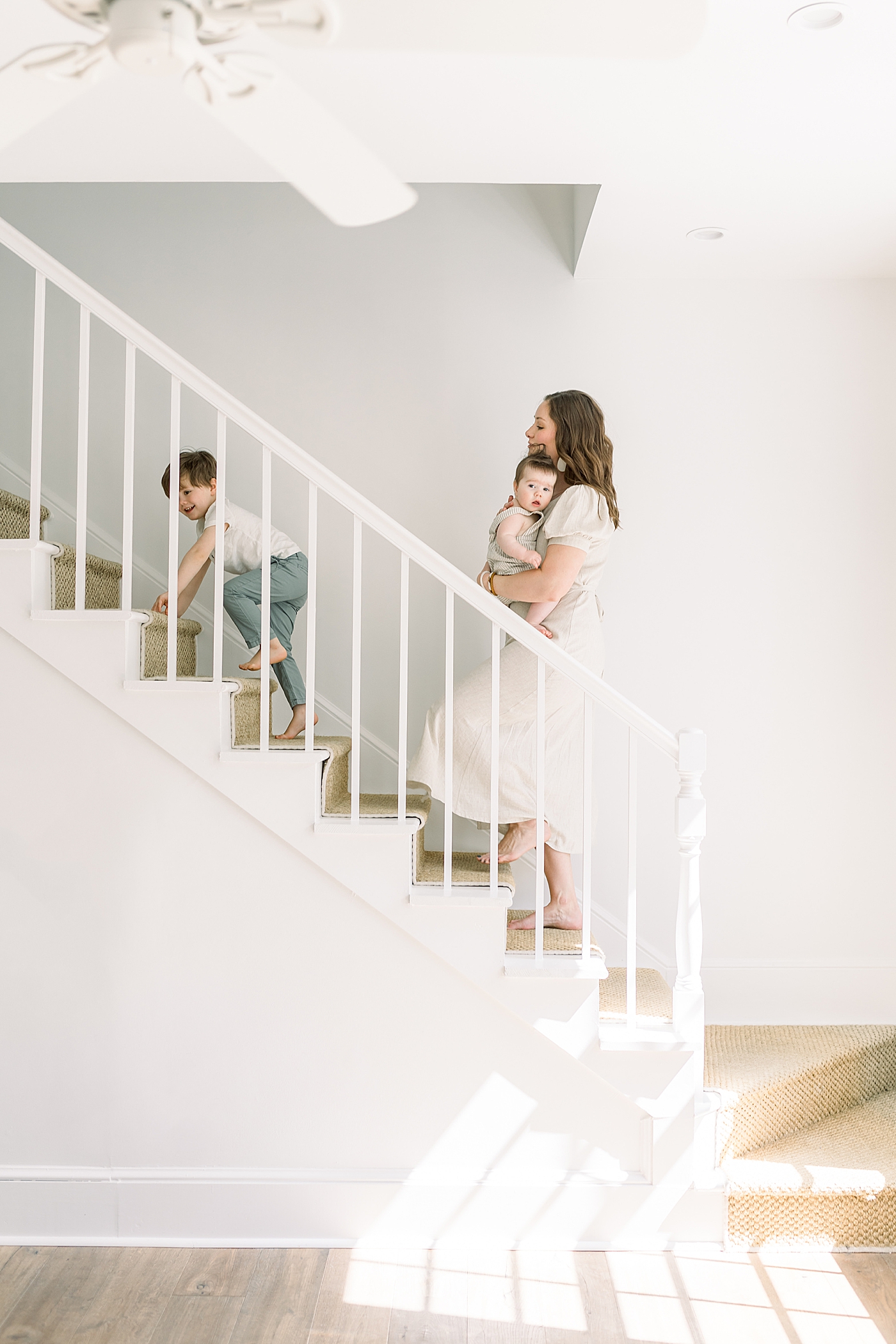Mother with her two children going up a simple, white staircase | Image by Caitlyn Motycka 