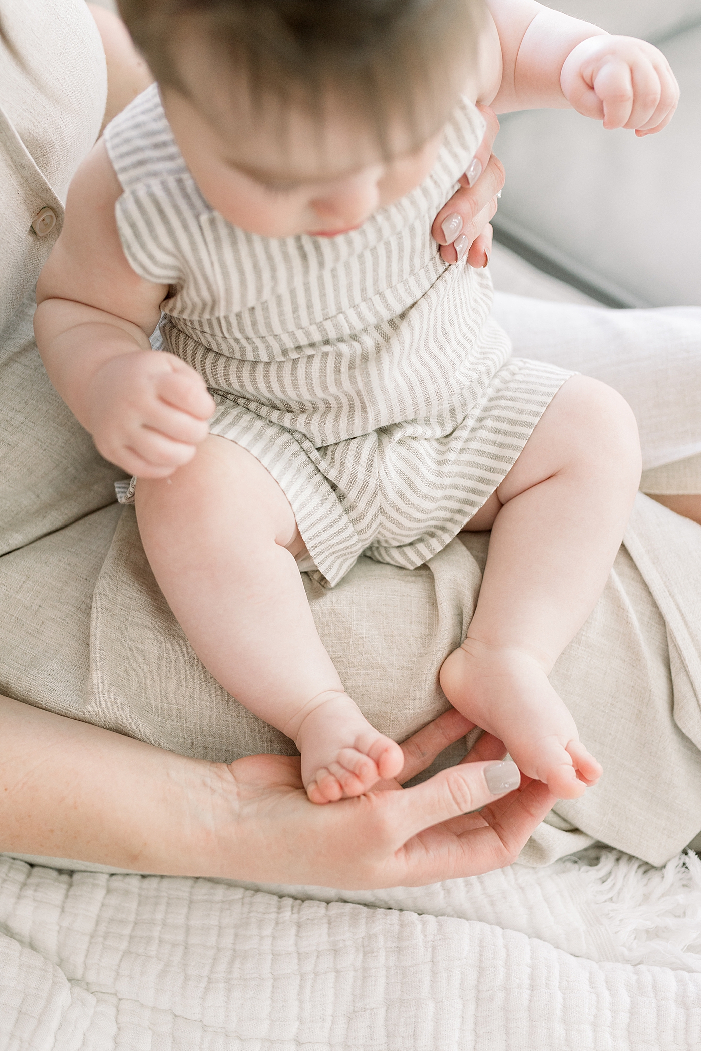 Close up of a child in a neutral-striped outfit sitting in mother's lap | Image by Caitlyn Motycka 