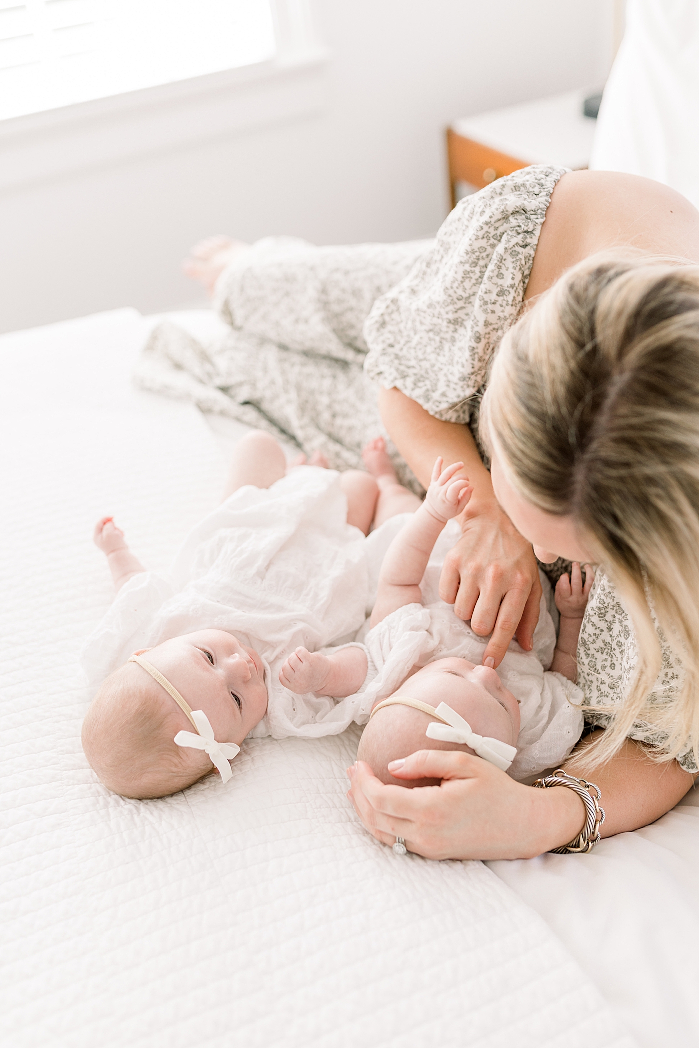 Close up of a mother in a spring dress holding twins on a bed with a neutral color palette | Image by Caitlyn Motycka 