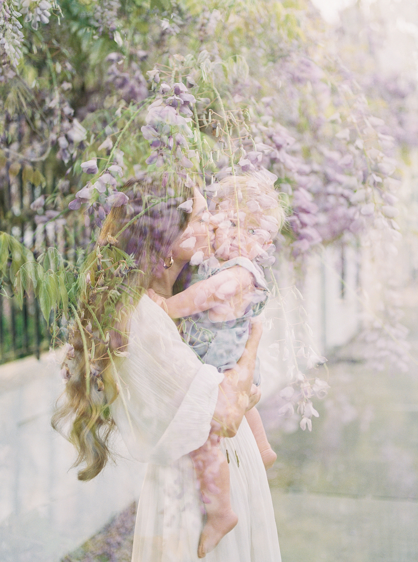 Double exposure image of mom holding her baby with wisteria in the background | Image by Caitlyn Motycka