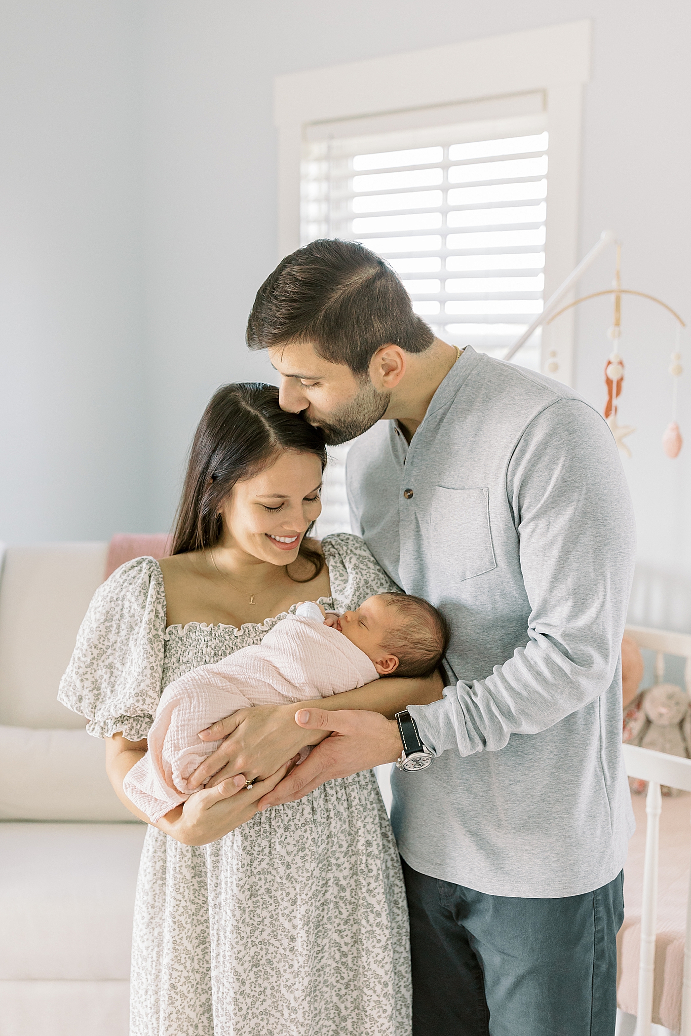 Mom and dad snuggling their baby in their nursery | Image by Caitlyn Motycka