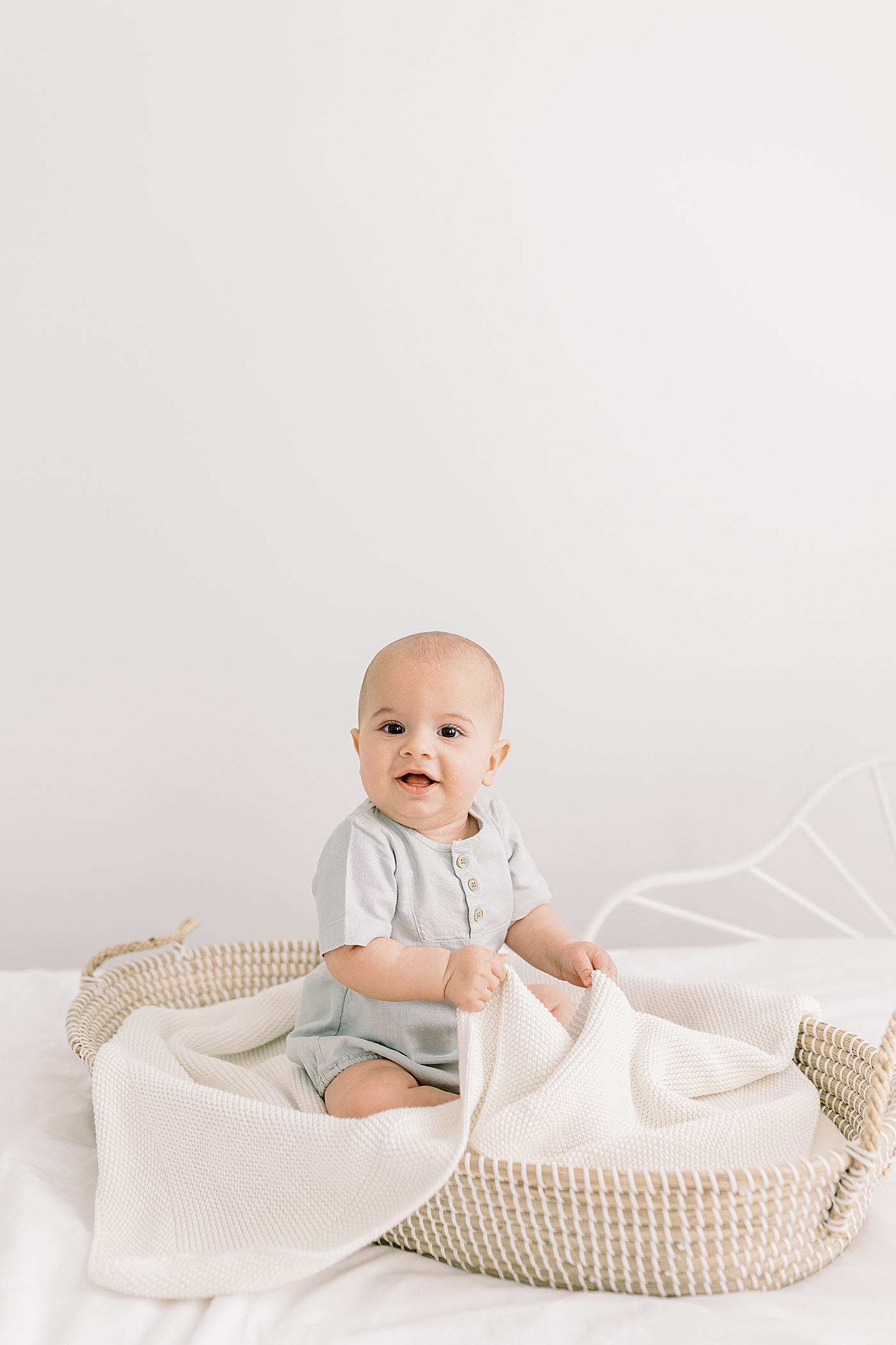 Baby sitting in a basket holding a wooden ship | Image by Caitlyn Motycka